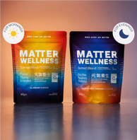 Two stand-up pouches of Matter Wellness supplement blends on a reflective surface against a warm gradient background. The left pouch is labeled Sunrise Blend Blueberry Flavour and has a red-to-blue gradient.